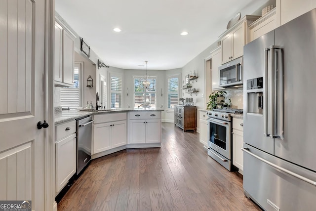 kitchen featuring dark wood-style flooring, high end appliances, light stone counters, a peninsula, and recessed lighting