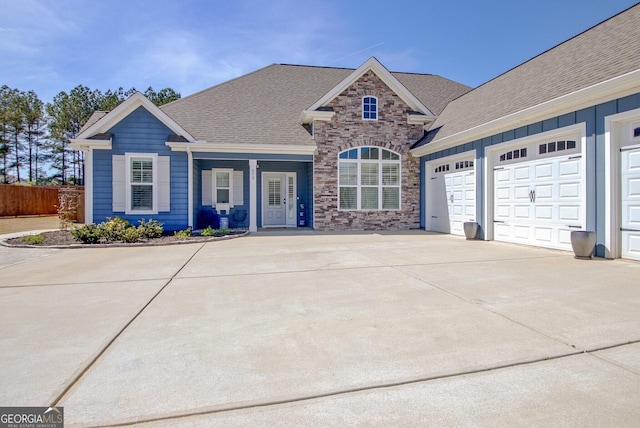 view of front of home featuring covered porch, driveway, fence, an attached garage, and stone siding