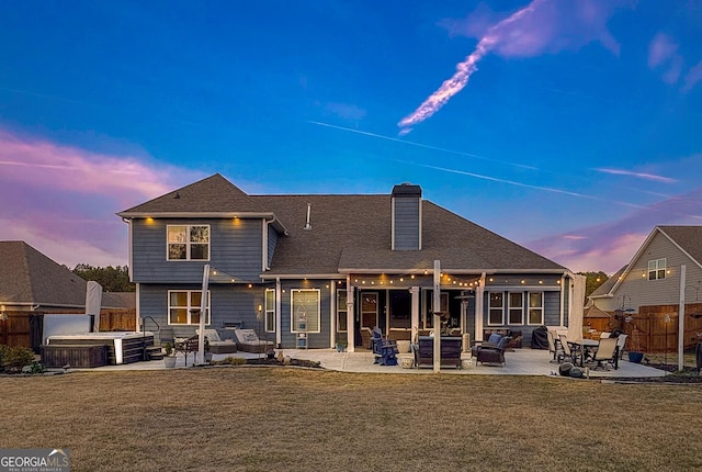 back of property at dusk featuring a lawn, a patio, fence, and a chimney