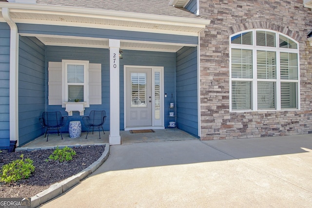 entrance to property featuring roof with shingles, a porch, and stone siding