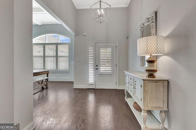 foyer featuring an inviting chandelier, ornamental molding, baseboards, and dark wood-style floors