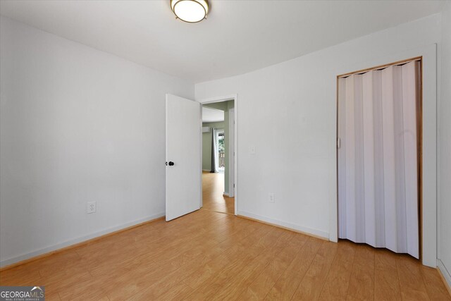 unfurnished bedroom featuring light wood finished floors, baseboards, and a closet