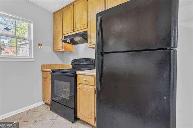 kitchen featuring light countertops, under cabinet range hood, baseboards, light tile patterned flooring, and black appliances
