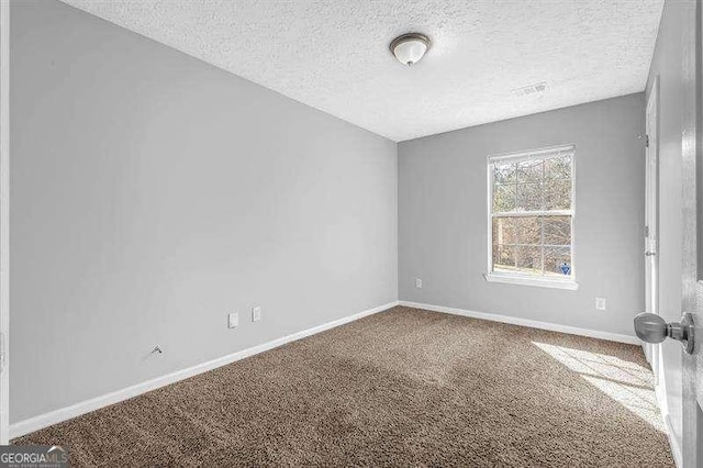 empty room with carpet flooring, visible vents, baseboards, and a textured ceiling