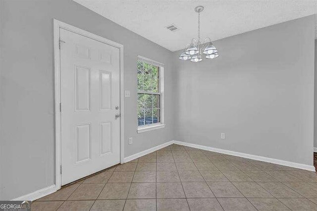 tiled foyer featuring baseboards, a textured ceiling, visible vents, and a notable chandelier