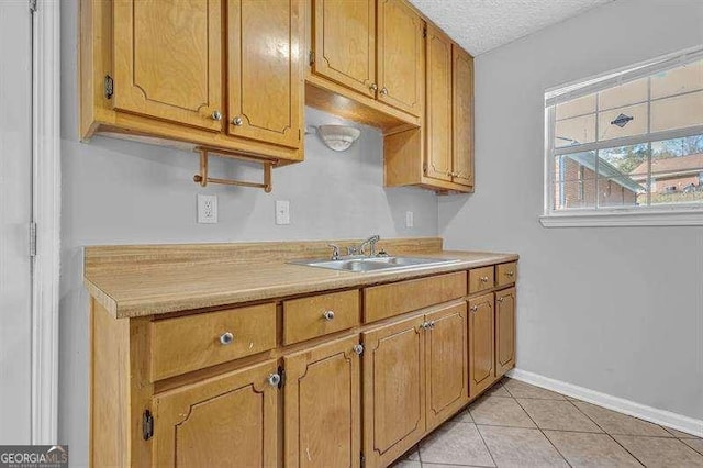 kitchen with a textured ceiling, light countertops, baseboards, a sink, and brown cabinetry