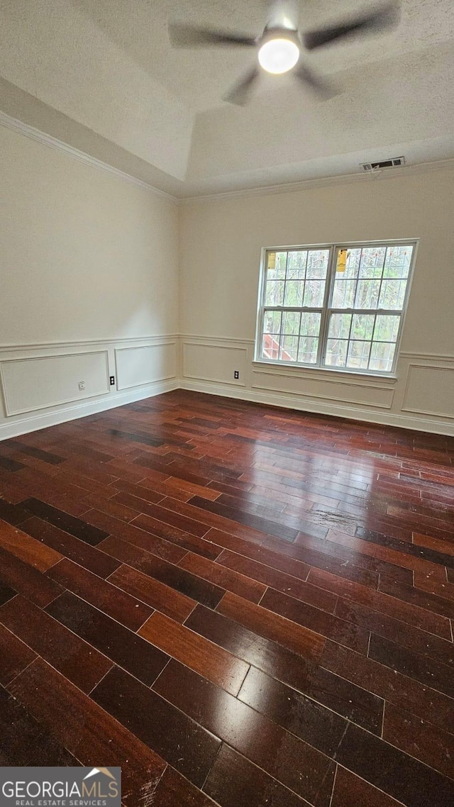 empty room with dark wood-style flooring, a textured ceiling, a wainscoted wall, visible vents, and a ceiling fan