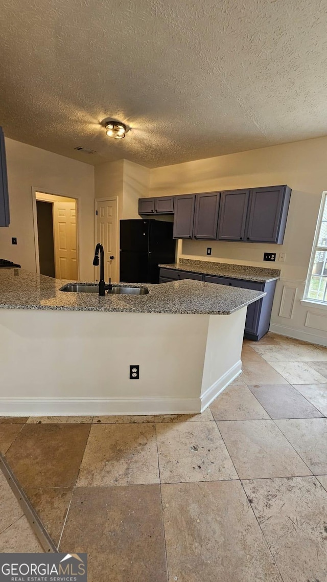 kitchen featuring a textured ceiling, light stone countertops, a sink, and freestanding refrigerator