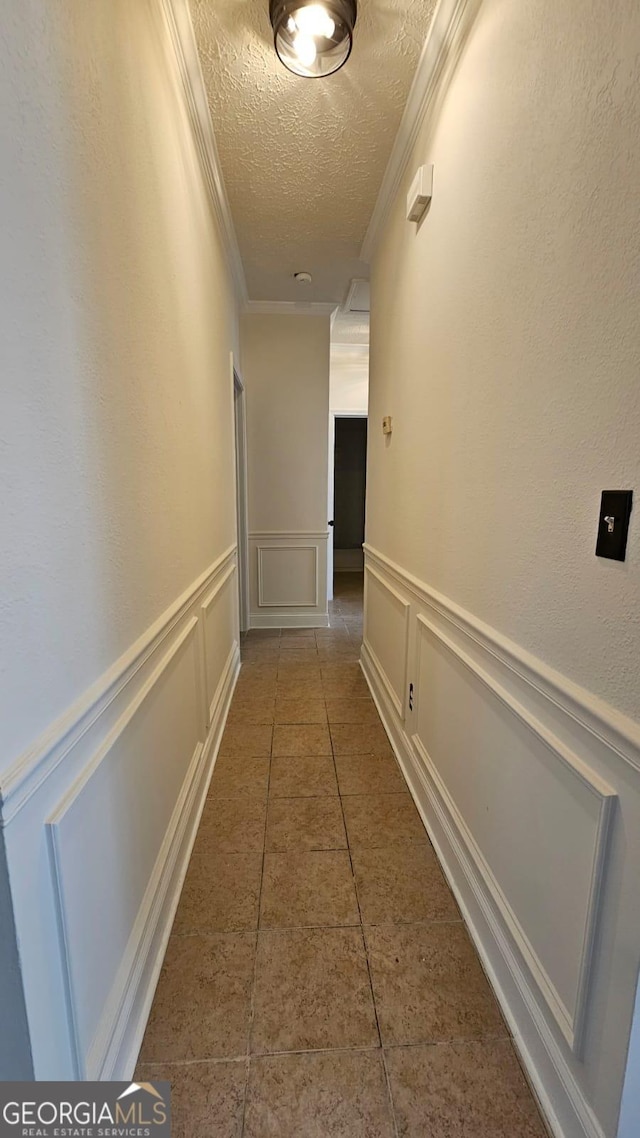 hallway featuring a decorative wall, ornamental molding, tile patterned floors, and a textured ceiling