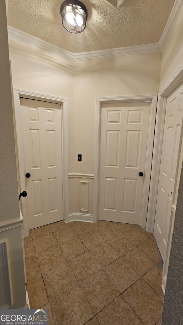 entryway with a textured ceiling, a wainscoted wall, ornamental molding, and a decorative wall
