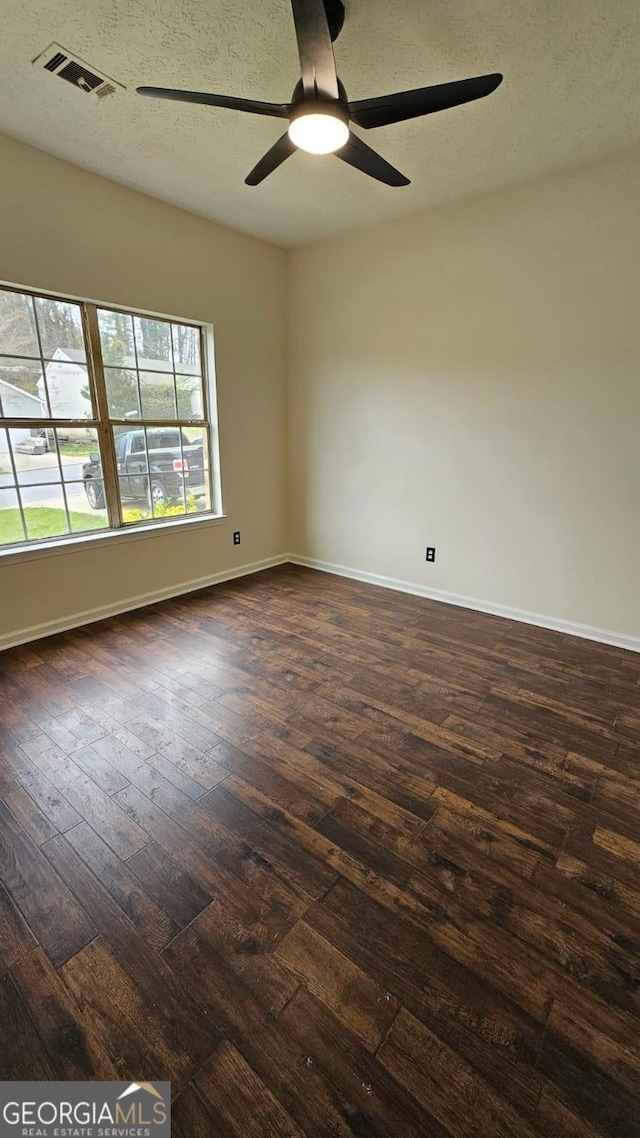 empty room with dark wood-style flooring, baseboards, ceiling fan, and visible vents