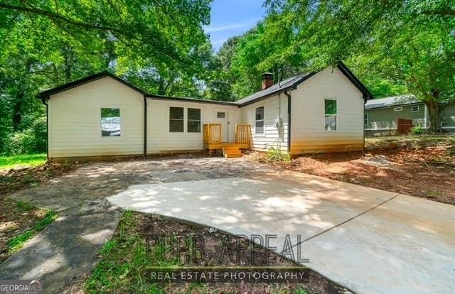 back of house featuring driveway, a chimney, and a patio area