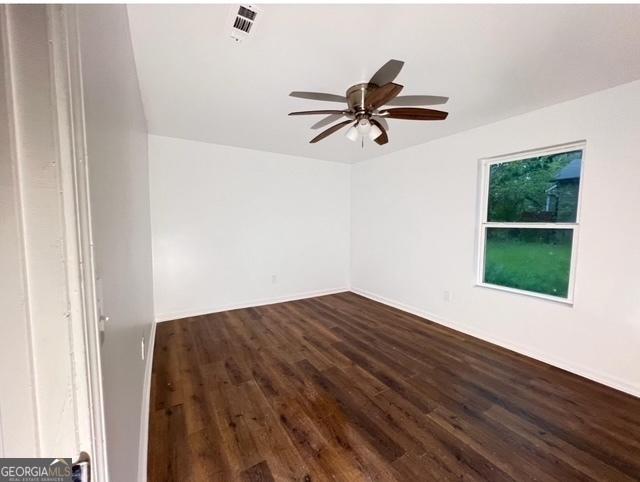 spare room with baseboards, visible vents, ceiling fan, and dark wood-style flooring