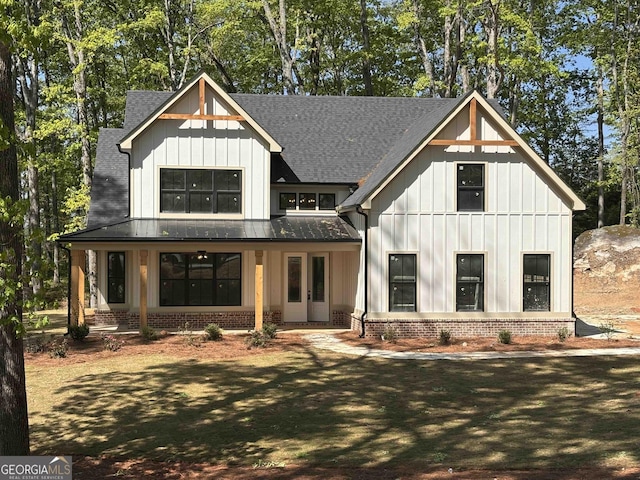 back of property with board and batten siding, a porch, brick siding, and roof with shingles