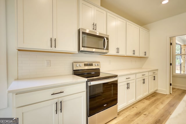kitchen with white cabinetry, backsplash, appliances with stainless steel finishes, and light wood finished floors