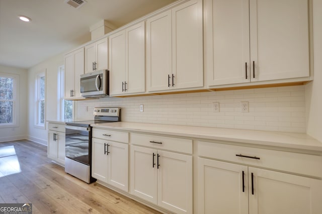 kitchen featuring light wood-type flooring, visible vents, appliances with stainless steel finishes, baseboards, and backsplash