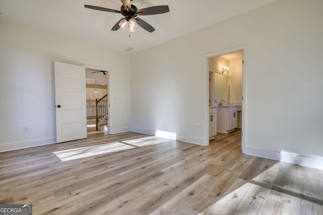 unfurnished bedroom featuring a sink, light wood finished floors, baseboards, and ensuite bathroom