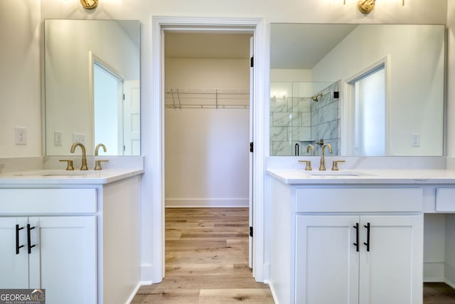 full bathroom featuring two vanities, a walk in closet, a stall shower, and wood finished floors