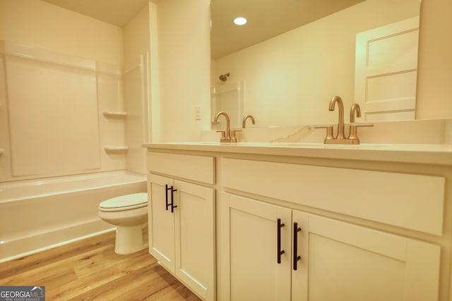 bathroom with recessed lighting, toilet, wood finished floors, a sink, and double vanity