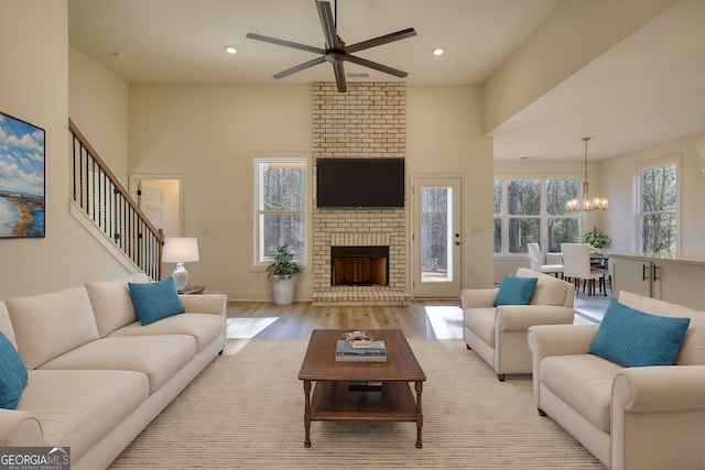 living room featuring a fireplace, recessed lighting, light wood-style floors, and ceiling fan with notable chandelier
