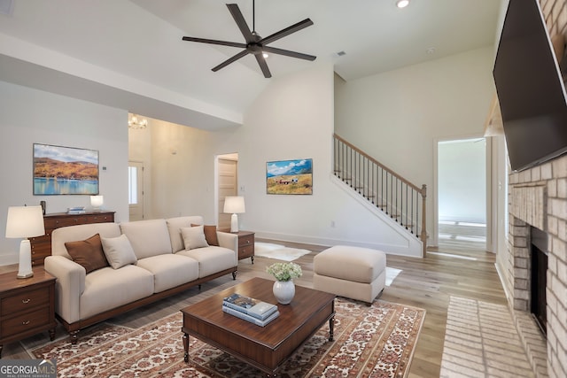 living room featuring visible vents, a ceiling fan, stairway, light wood-style flooring, and high vaulted ceiling