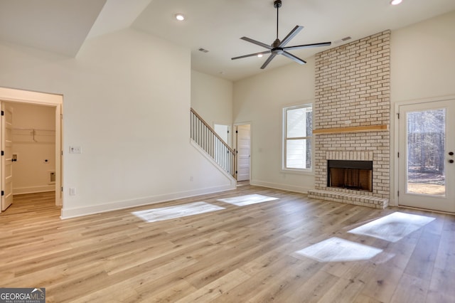 unfurnished living room with baseboards, a brick fireplace, ceiling fan, light wood-style floors, and high vaulted ceiling