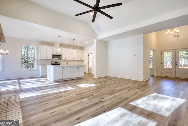 unfurnished living room with light wood-type flooring, recessed lighting, plenty of natural light, and ceiling fan with notable chandelier