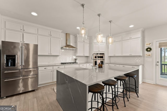 6635 Canyon Cv, Cumming, GA 30028 - kitchen featuring white cabinets, backsplash, light wood-style floors, wall chimney exhaust hood, and appliances with stainless steel finishes