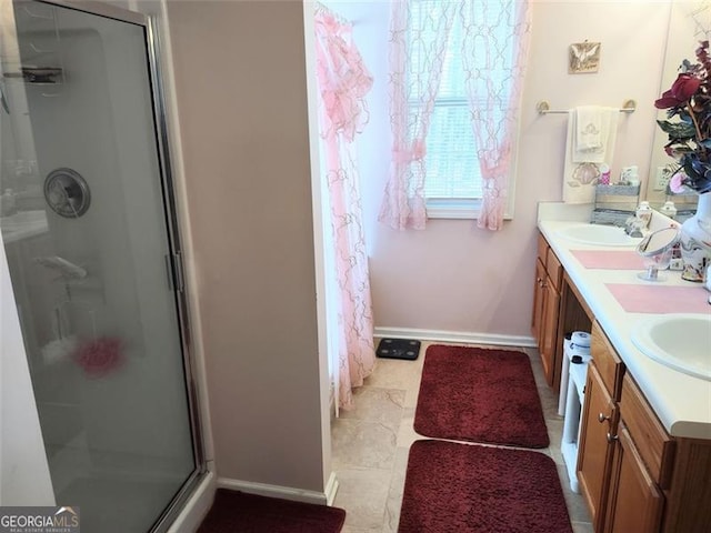 full bath featuring double vanity, a sink, a shower stall, and baseboards