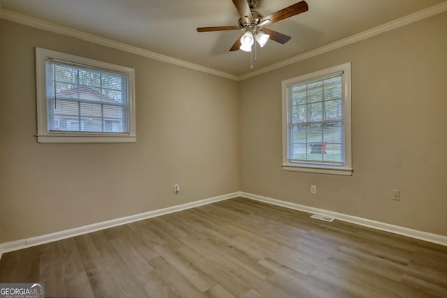 empty room featuring wood finished floors, crown molding, baseboards, and visible vents