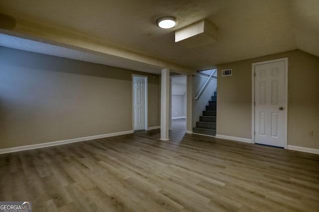 finished below grade area featuring baseboards, visible vents, wood finished floors, and stairway