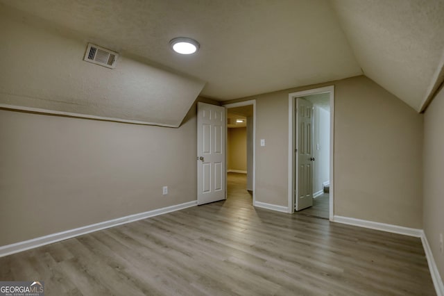 bonus room featuring baseboards, a textured ceiling, visible vents, and wood finished floors