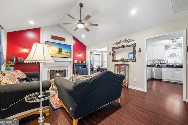 living area featuring vaulted ceiling, dark wood finished floors, a large fireplace, visible vents, and a ceiling fan