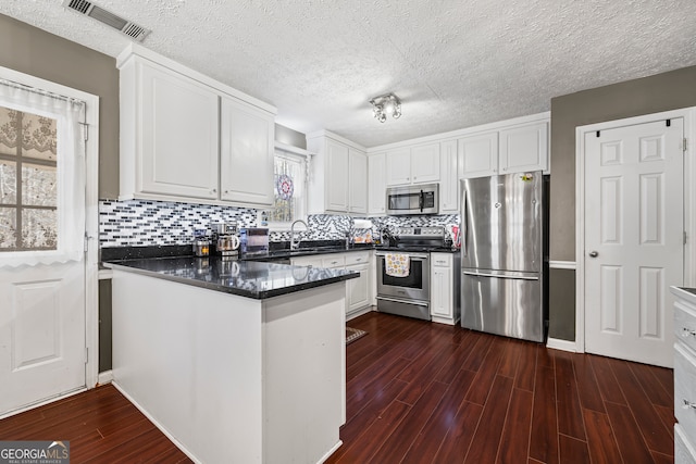 kitchen with dark countertops, a peninsula, white cabinetry, and stainless steel appliances