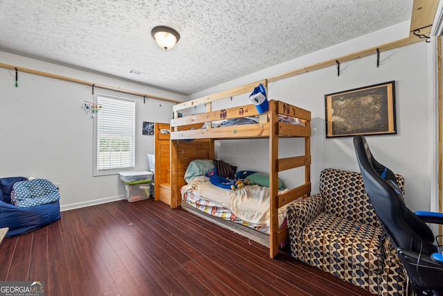 bedroom with baseboards, visible vents, wood finished floors, and a textured ceiling