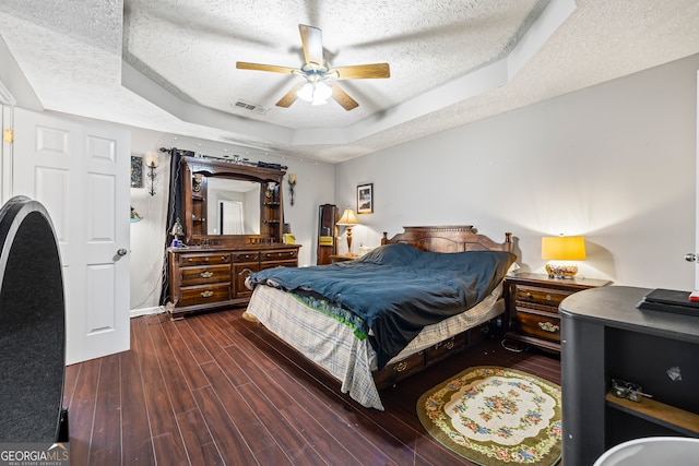 bedroom with a textured ceiling, visible vents, ceiling fan, wood finished floors, and a tray ceiling
