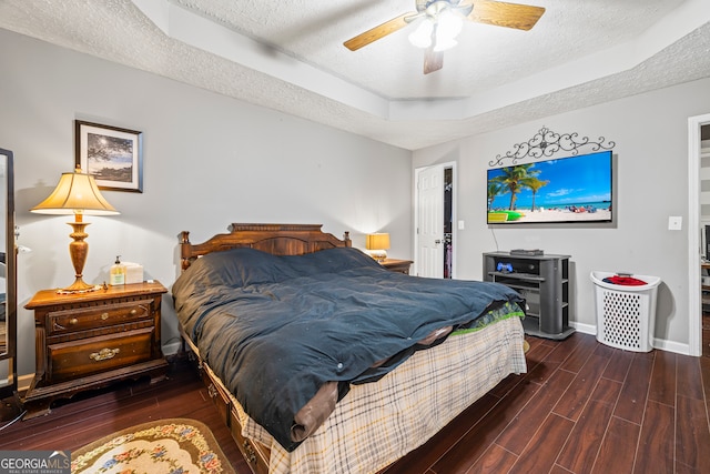 bedroom featuring a textured ceiling, baseboards, wood finished floors, a ceiling fan, and a raised ceiling