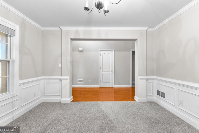 spare room with a decorative wall, visible vents, carpet, ornamental molding, and an inviting chandelier
