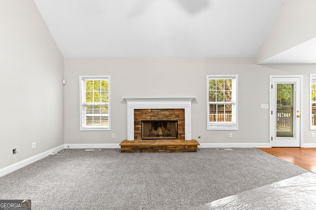 unfurnished living room with baseboards, lofted ceiling, carpet floors, and a stone fireplace