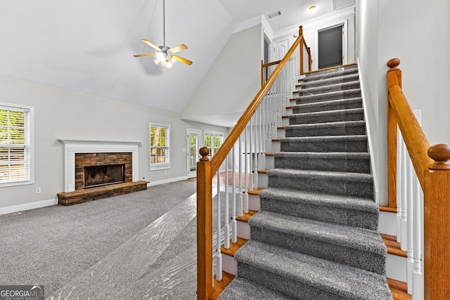 stairway with high vaulted ceiling, visible vents, baseboards, a ceiling fan, and a stone fireplace