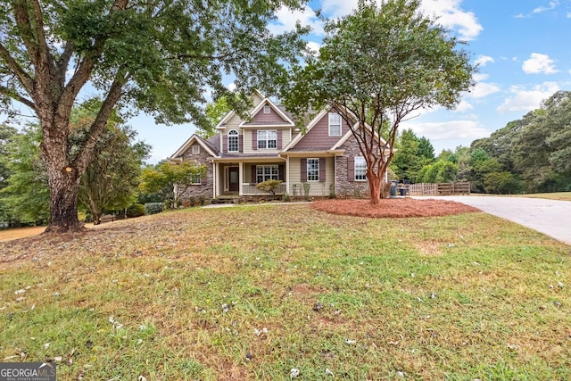 view of front facade with stone siding, a front yard, concrete driveway, and fence