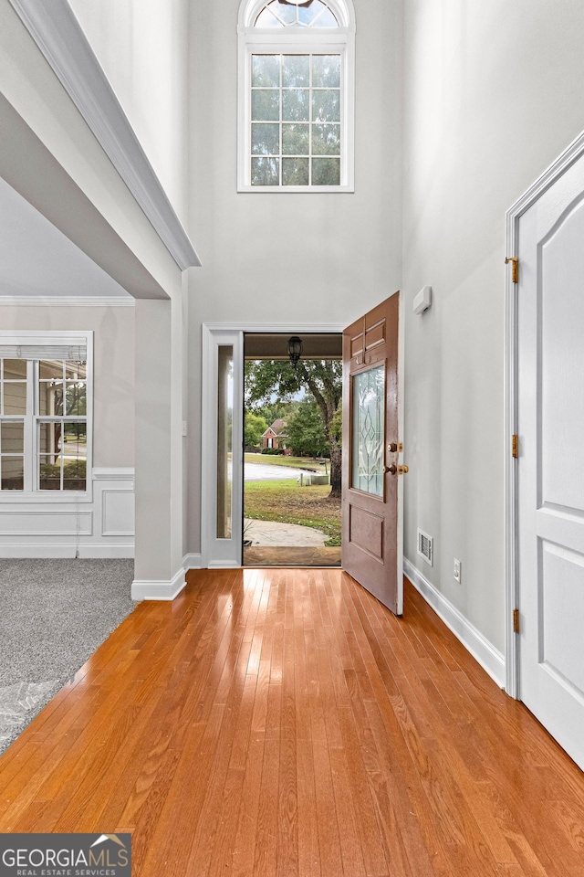 foyer entrance featuring hardwood / wood-style floors, a towering ceiling, visible vents, and wainscoting