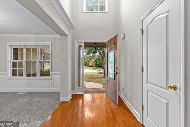 foyer entrance with a decorative wall, light wood-style flooring, plenty of natural light, and crown molding