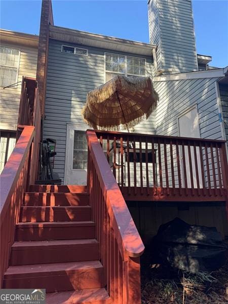 rear view of property featuring a chimney, stairs, and a wooden deck