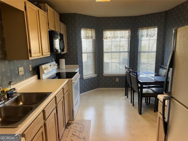 kitchen featuring light countertops, white appliances, wallpapered walls, a sink, and light floors