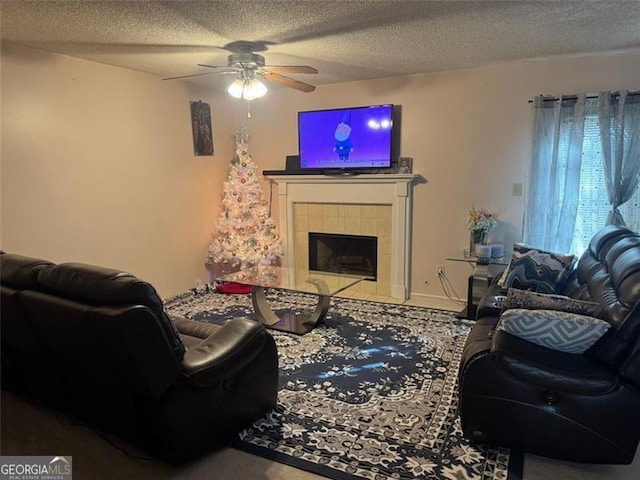 living area with a textured ceiling, a tiled fireplace, and a ceiling fan