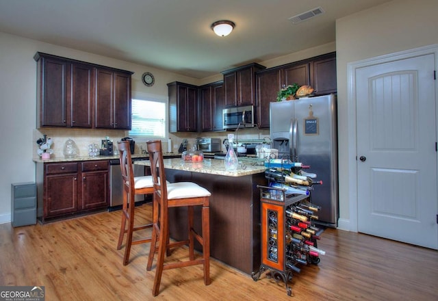kitchen with a kitchen breakfast bar, visible vents, appliances with stainless steel finishes, dark brown cabinets, and light wood-style floors