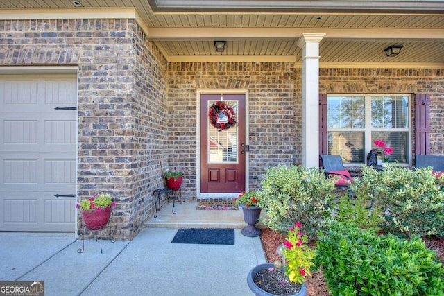 view of exterior entry with brick siding, a garage, and covered porch