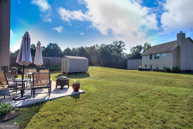 view of yard featuring an outdoor structure, a fire pit, fence, a patio, and a storage unit
