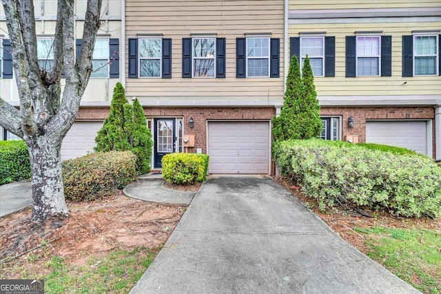 view of property with an attached garage, driveway, and brick siding